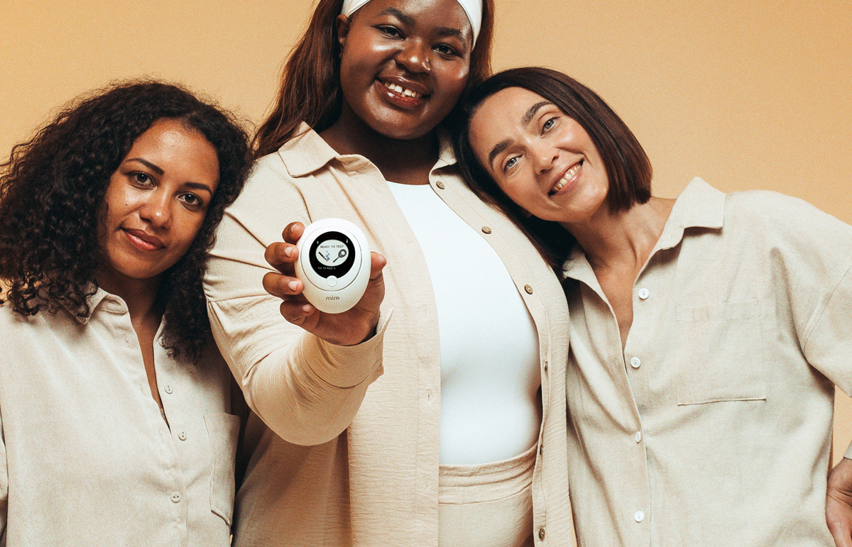Three diverse women smiling and holding a Mira Fertility hormone monitor tracker device displaying Ready to Test screen