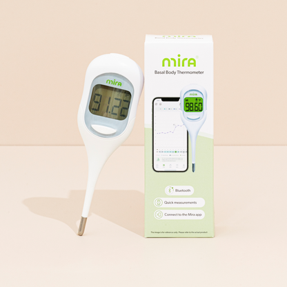 White Mira basal body thermometer with digital display next to packaging box showing smartphone app interface.