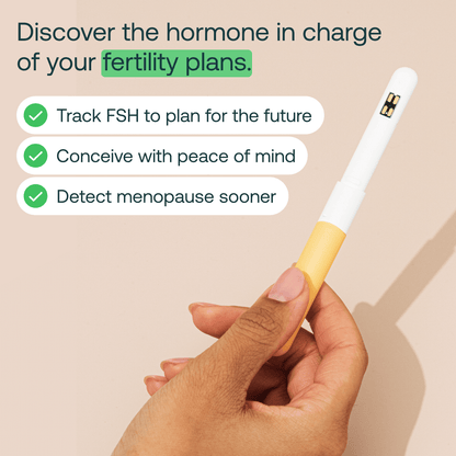 White and yellow handheld fertility tracking device with digital display held in hand against beige background.