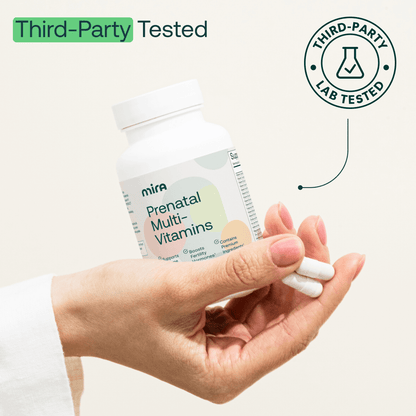 Hand holding white Mira Prenatal Multi-Vitamins bottle with two capsules, third-party lab tested seal visible.