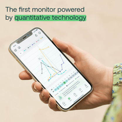 Hand holding smartphone displaying hormone tracking app with colorful line graphs and data charts on screen.