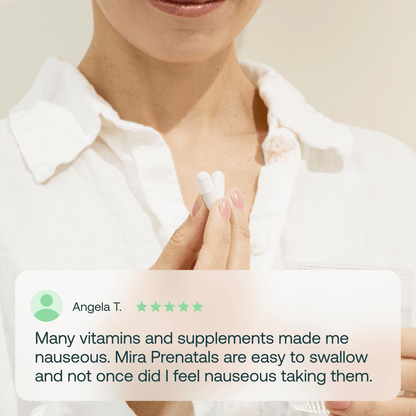 Person in white shirt holding two white prenatal vitamin pills in palm of hand.