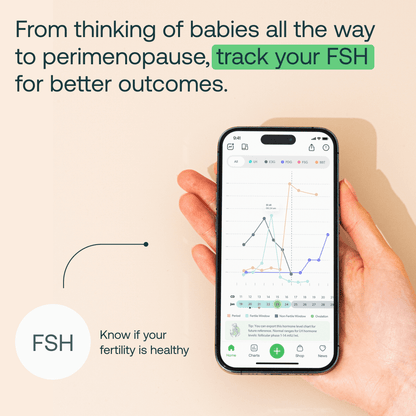Hand holding smartphone displaying FSH tracking app with hormone level charts and fertility data graphs.