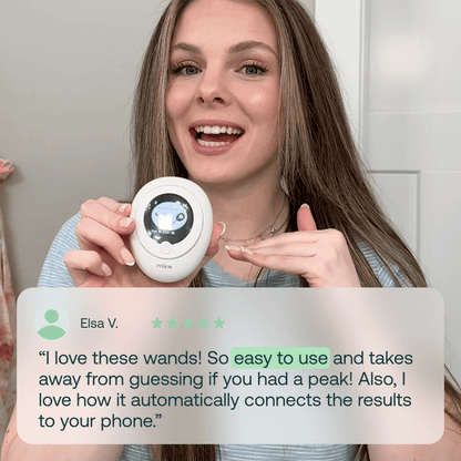 White handheld fertility tracking device with digital display held by a person with long brown hair.