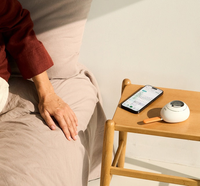 Mira Fertility Monitor and app on bedside table next to person resting in bed, tracking hormone data for fertility awareness