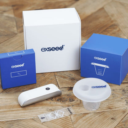 ExSeed Sperm 2 test kit components including white and blue packaging, white analyzer device, collection cup, and instruction