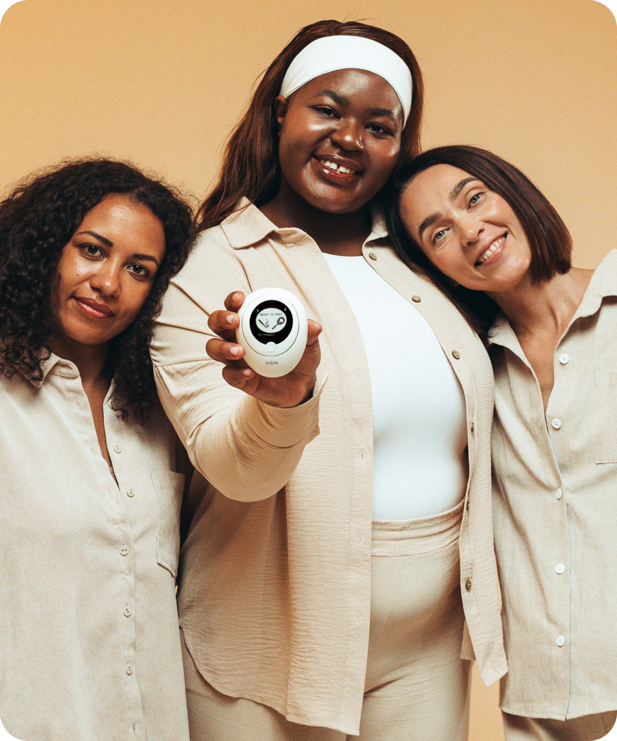 Three diverse women smiling and holding a Mira Fertility hormone monitor tracker device displaying Ready to Test screen
