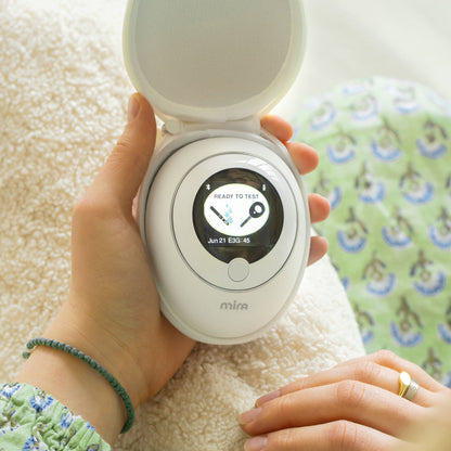 White Mira device with digital display showing "Ready to Test" held in hand, displaying date and time.
